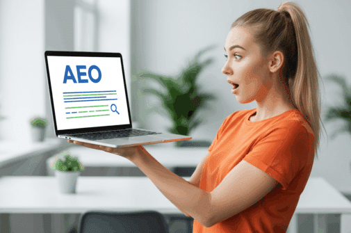 Eine junge Frau mit Pferdeschwanz schaut erstaunt, während sie ihr Laptop hochhält. Auf dem Bildschirm sind neben stilisierten Suchergebnissen die Buchstaben „AEO” groß zu sehen. Sie trägt ein orangefarbenes T-Shirt. Der stilvoll-moderne Hintergrund ist aufgrund der Tiefenschärfe leicht unscharf. Stil: fotorealistisch. Beachten Sie den Goldenen Schnitt. Das Hauptmotiv befindet sich auf der rechten Seite.